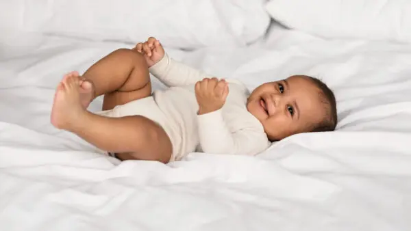 Een foto van een glimlachende baby op een bed.